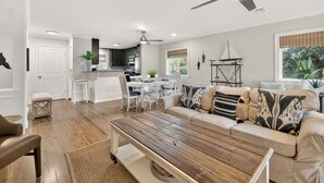 A modern living room with a wooden coffee table, beige sofa, and a dining area with white chairs.
