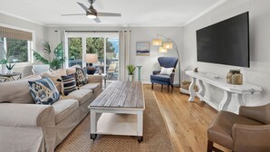 A living room with a sofa, coffee table, and armchairs, a flat-screen TV, and a ceiling fan.