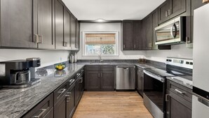 A modern kitchen with dark cabinets, a stainless steel dishwasher, a built-in oven, and a microwave.