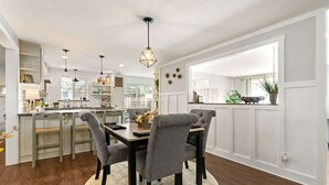 A modern kitchen with white cabinetry, a dining area with a round table and grey upholstered chairs, and pendant lighting.