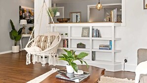 A modern living room with a hanging chair, a wooden coffee table, and a white bookshelf filled with books and decorative items.
