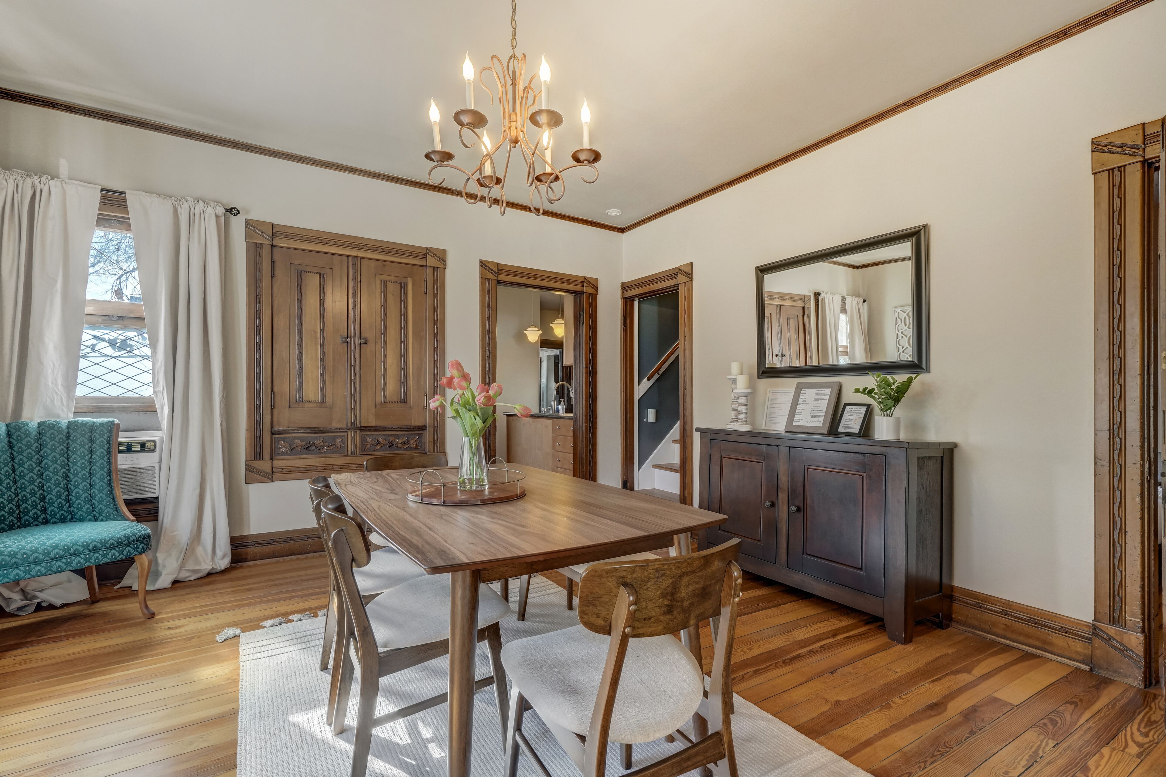 A dining room with a wooden table, chairs, a chandelier, and a view of the outside through large windows.