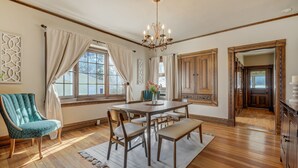 A dining area with a wooden table, chairs, and a bench. There is a chandelier above the table, and the room has wooden floors and walls.