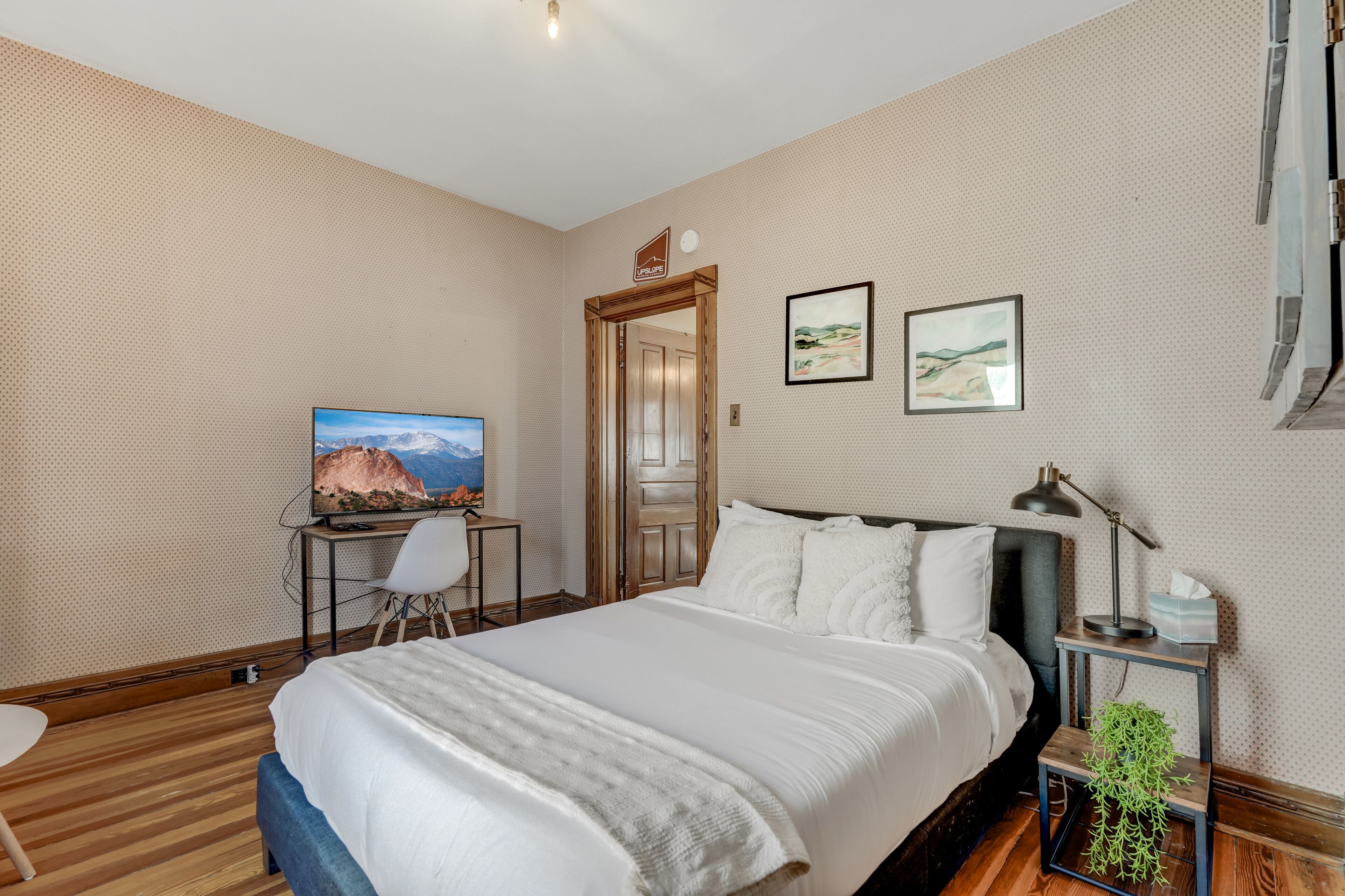 A bedroom with a bed, a desk with a TV, a chair, and two framed pictures on the wall.