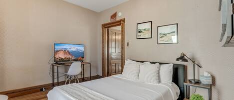 A bedroom with a bed, a desk with a TV, a chair, and two framed pictures on the wall.