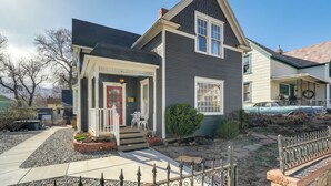 A two-story house with a dark gray exterior, a red door, and a small front porch with white chairs.