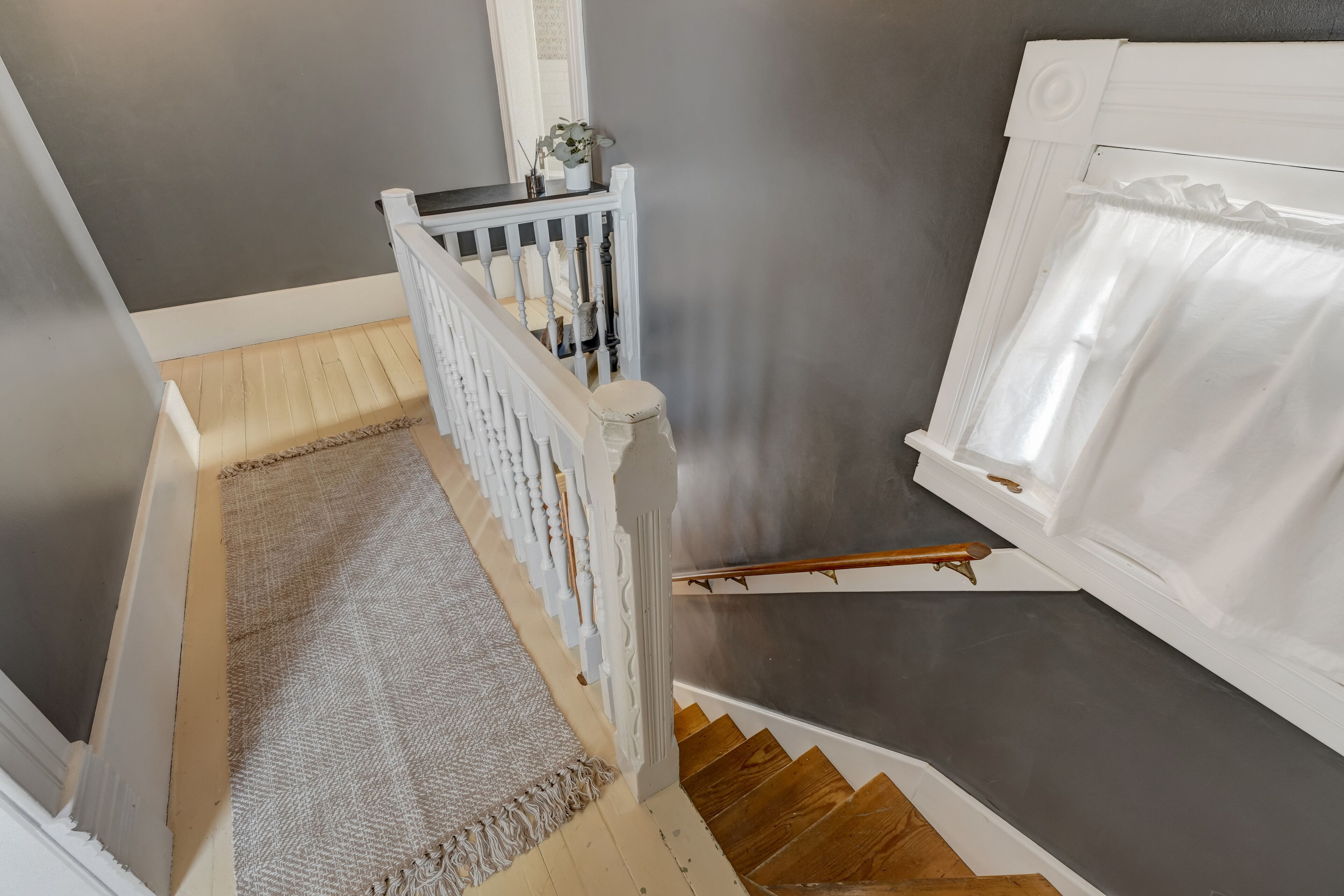 Un escalier avec une rampe blanche, une main courante en bois et un tapis beige.