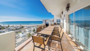 Balcón con mesa y sillas con vista a una playa y al paisaje urbano.