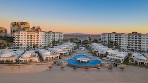 Un resort con varias edificaciones, una piscina central y una zona de playa.