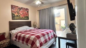 Une chambre à coucher avec un lit, un ventilateur de plafond, un tableau, une fenêtre avec des rideaux et un bureau avec une lampe.
