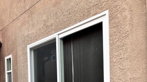 Une porte-fenêtre à glissière avec un cadre blanc, un paillasson et une plante en pot placés à côté.