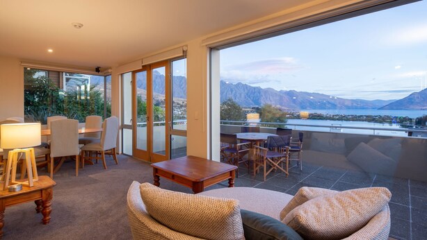 Un grand balcon offrant une vue sur les montagnes et un lac, aménagé avec une table, des chaises et un canapé.