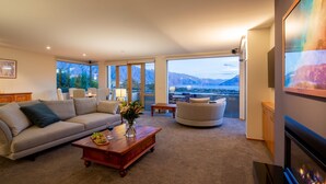 Un salon spacieux comprenant un canapé, un fauteuil et une table basse. De grandes fenêtres offrent une vue sur les montagnes et un lac.