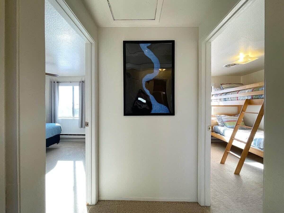A hallway with a framed artwork, a bunk bed, and a door leading to another room.