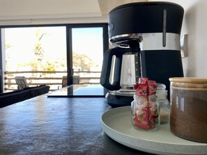 A coffee maker on a table with a glass jar and a packet of coffee creamer.
