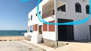Un edificio moderno de dos plantas con balcón, paredes blancas y vista al mar.
