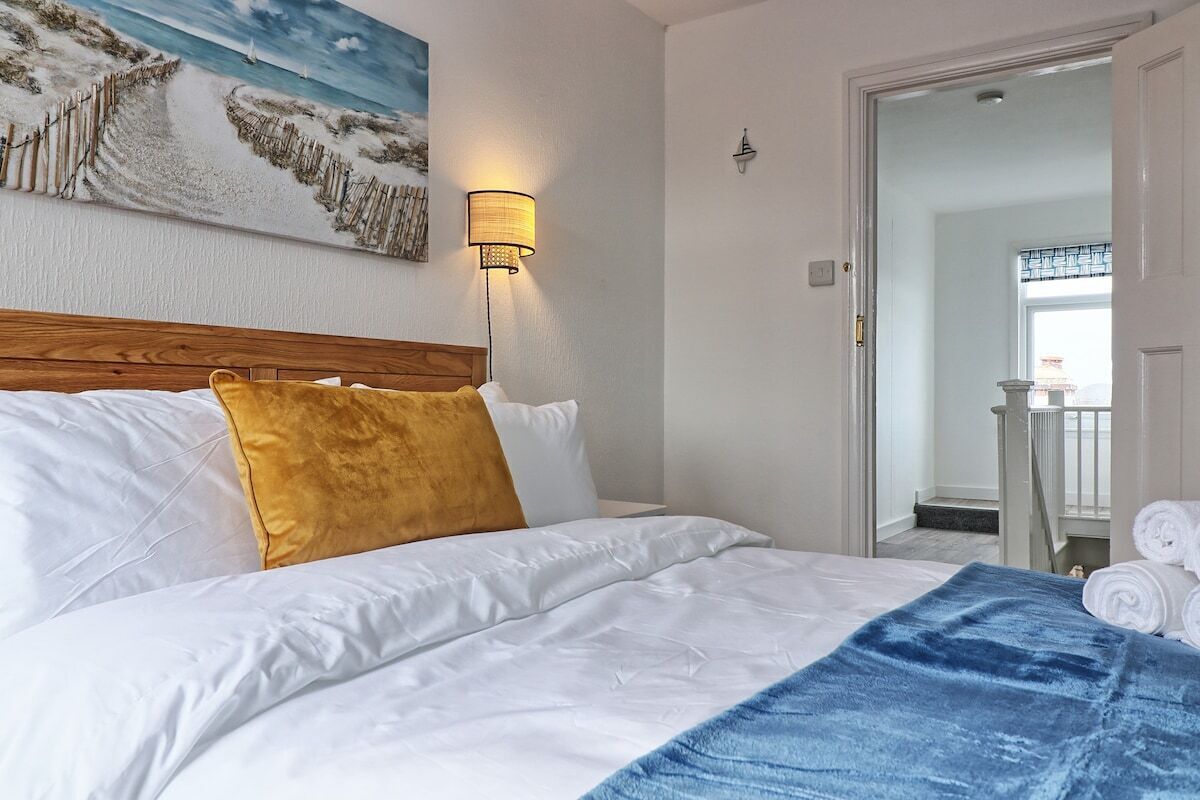 Habitación de hotel con cama, lámpara de pared, un cuadro de una escena de playa y vistas a un balcón con toallas.