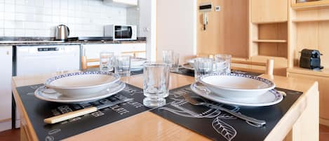 A dining table set with plates, glasses, and cutlery, with a microwave and kettle in the background.