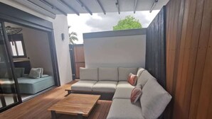 Ein moderner Außenbereich mit Holzterrasse, einer hellen Couch und einem Holztisch.