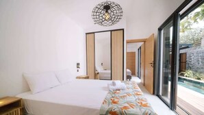 Ein modernes Schlafzimmer mit einem großen Bett, einem Nachttisch aus Holz, einem Spiegel und Blick auf einen Swimmingpool durch große Glasfenster.
