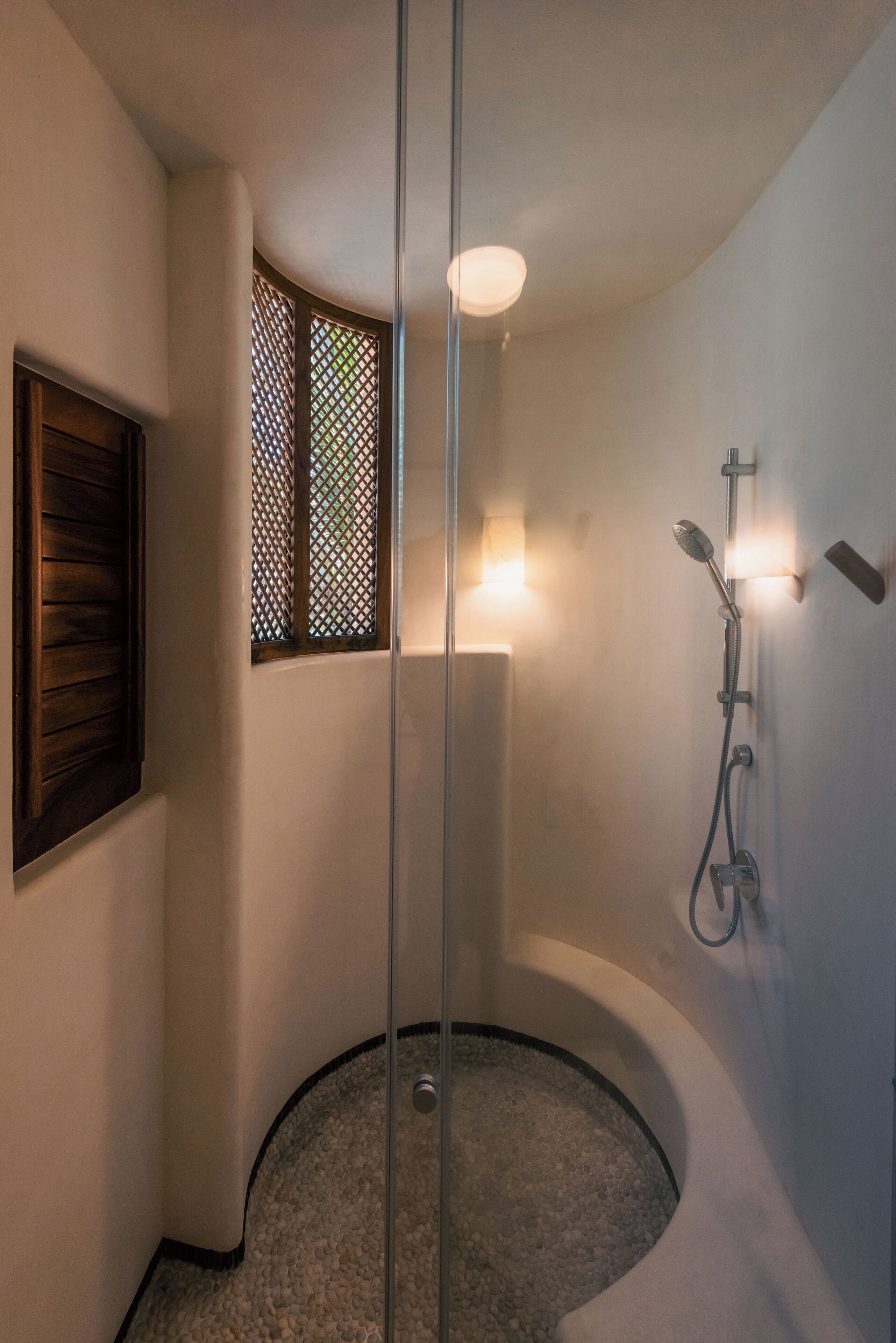 A modern bathroom with a glass-enclosed shower, a wooden door, and a window with a lattice design.