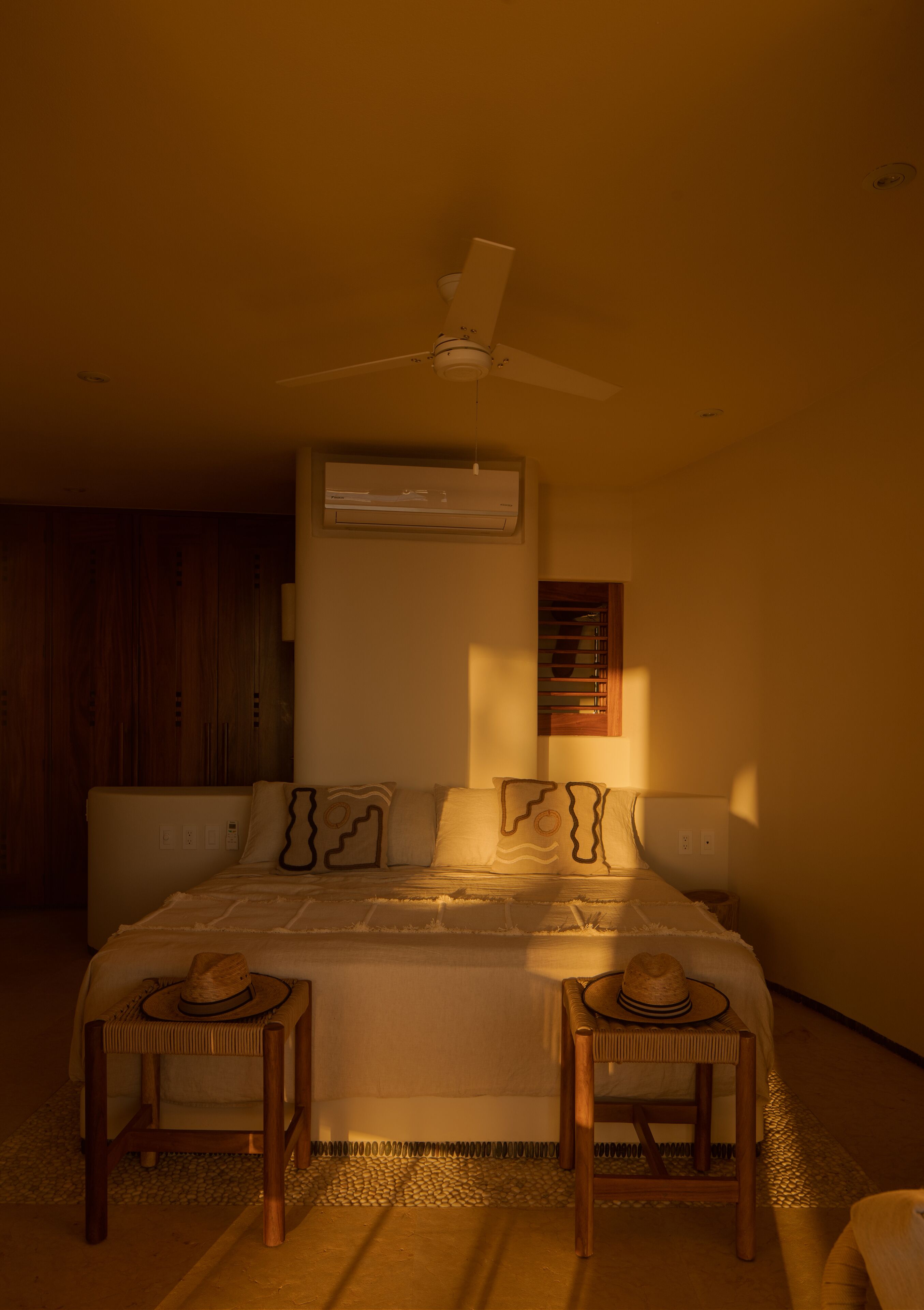 A bedroom with a bed, two nightstands, a ceiling fan, an air conditioning unit, and a window with blinds.