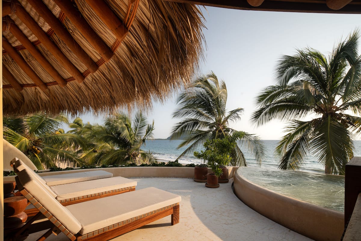 Een strandlounge met rieten dak, palmbomen en uitzicht op de oceaan.