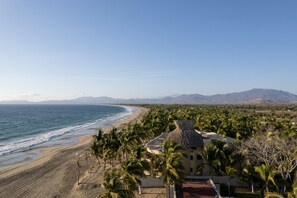 Un resort frente a la playa, con vista al océano, palmeras y montañas al fondo.
