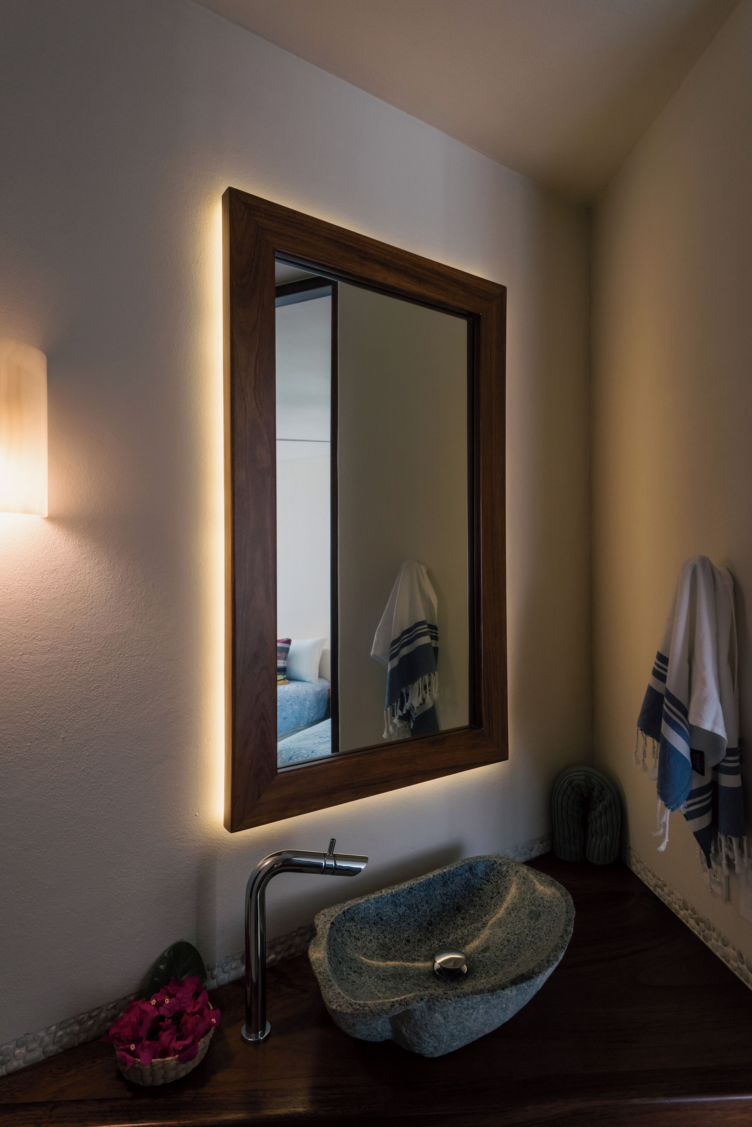 Un baño con un lavamanos de piedra, un espejo con marco de madera y un perchero para toallas.