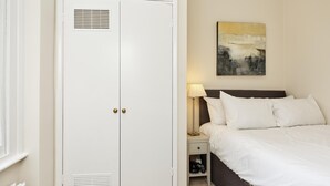Hotellihuone, jossa on sänky, yöpöytä, lamppu, vaatekaappi ja taulu seinällä.