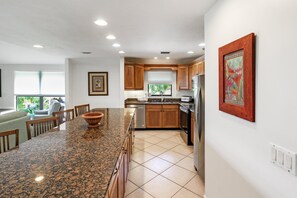 A modern kitchen with granite countertops, wooden cabinets, stainless steel appliances, and a dining area with a large island. - 3BR Villa with rooftop sundeck, gulf views and private beach - pet friendly - Signal Inn 16 (Sanibel)