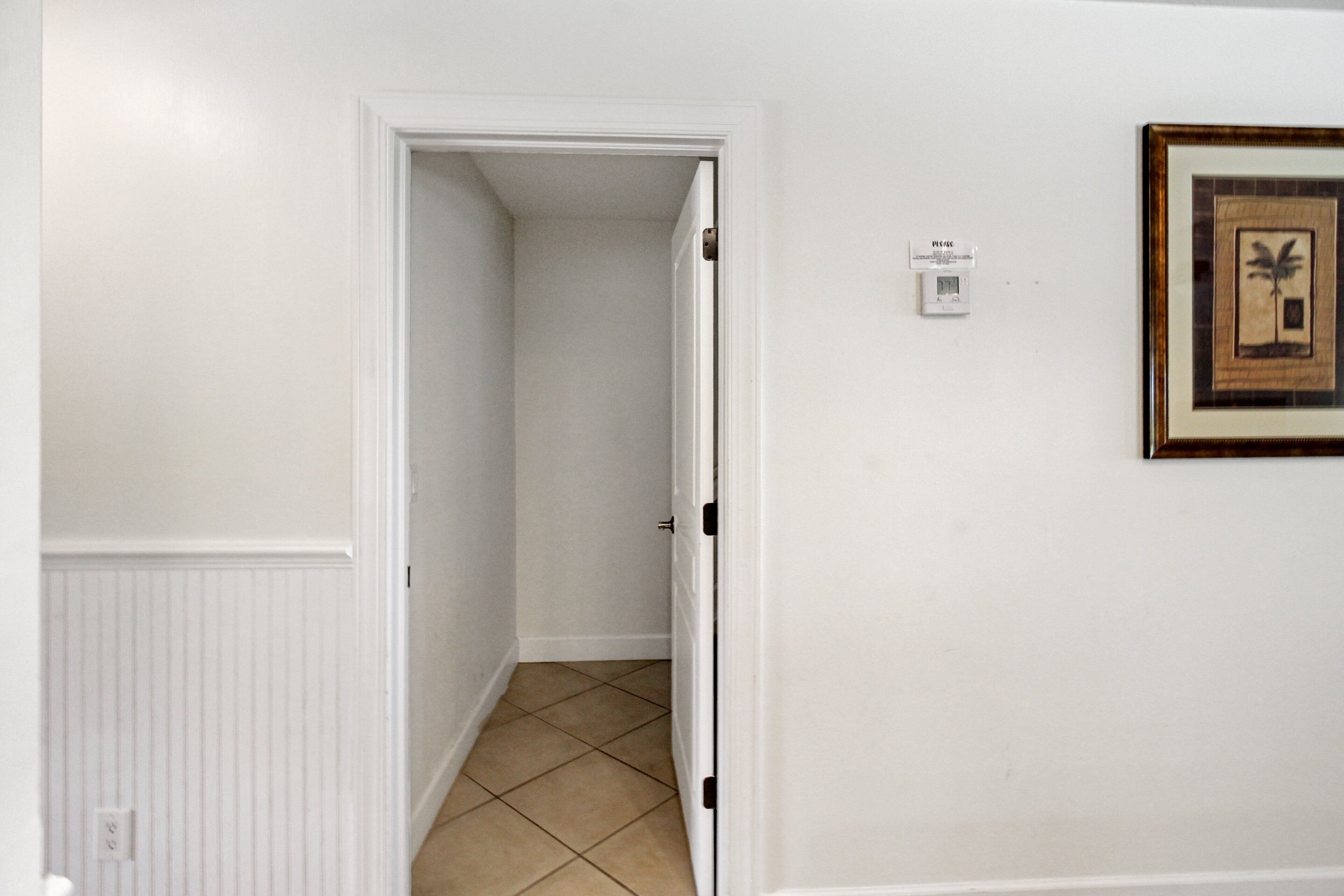 Ein Flur mit einer zur Tür geöffneten Zimmertür, einem gerahmten Bild an der Wand und einem Thermostat.
