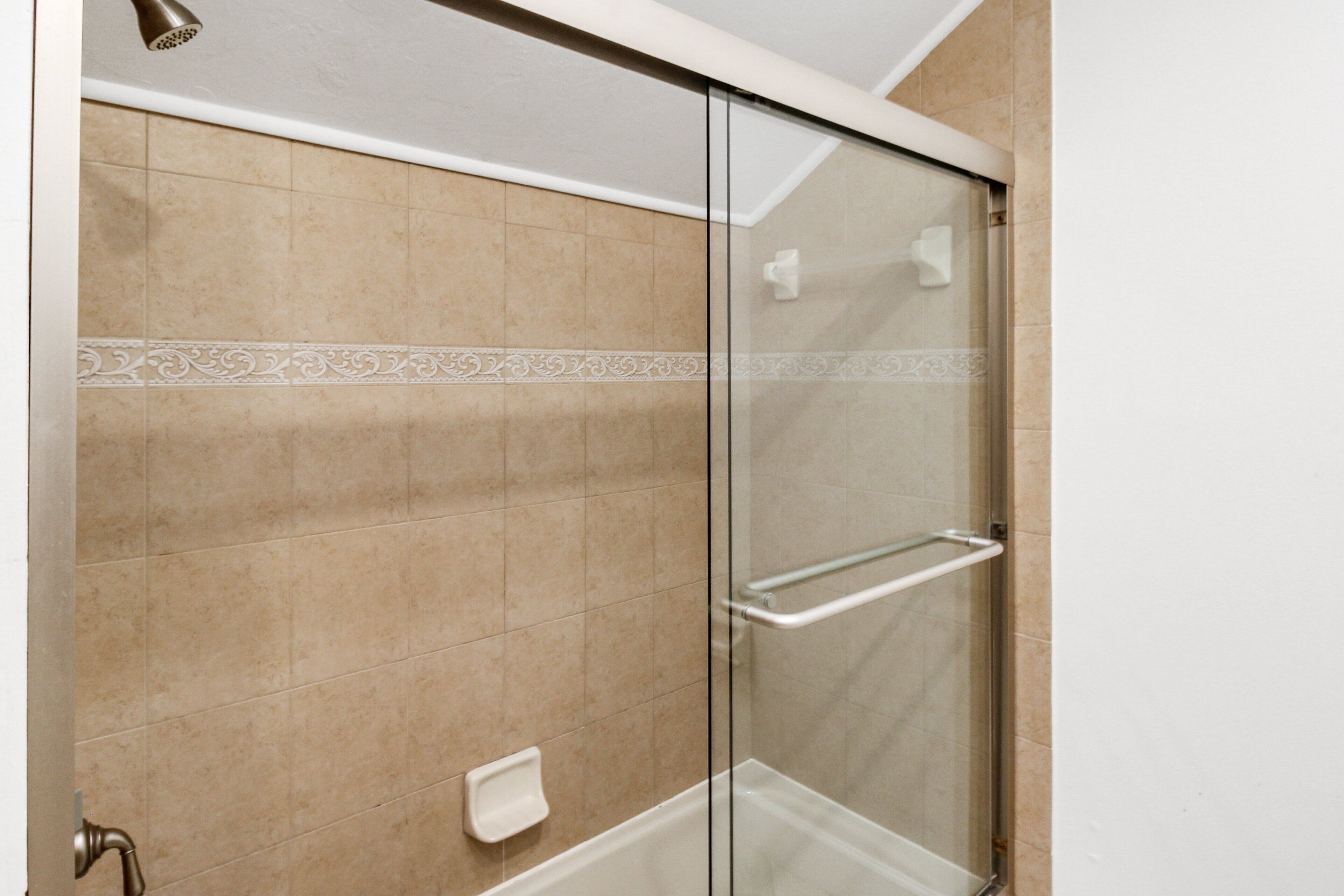 A glass-enclosed shower with beige tiles and a white decorative border.