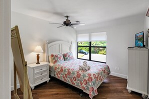 A bedroom with a bed, a nightstand, a lamp, a ceiling fan, a window with a view, and a TV on a stand. - 3BR Villa with rooftop sundeck, gulf views and private beach - pet friendly - Signal Inn 16 (Sanibel)