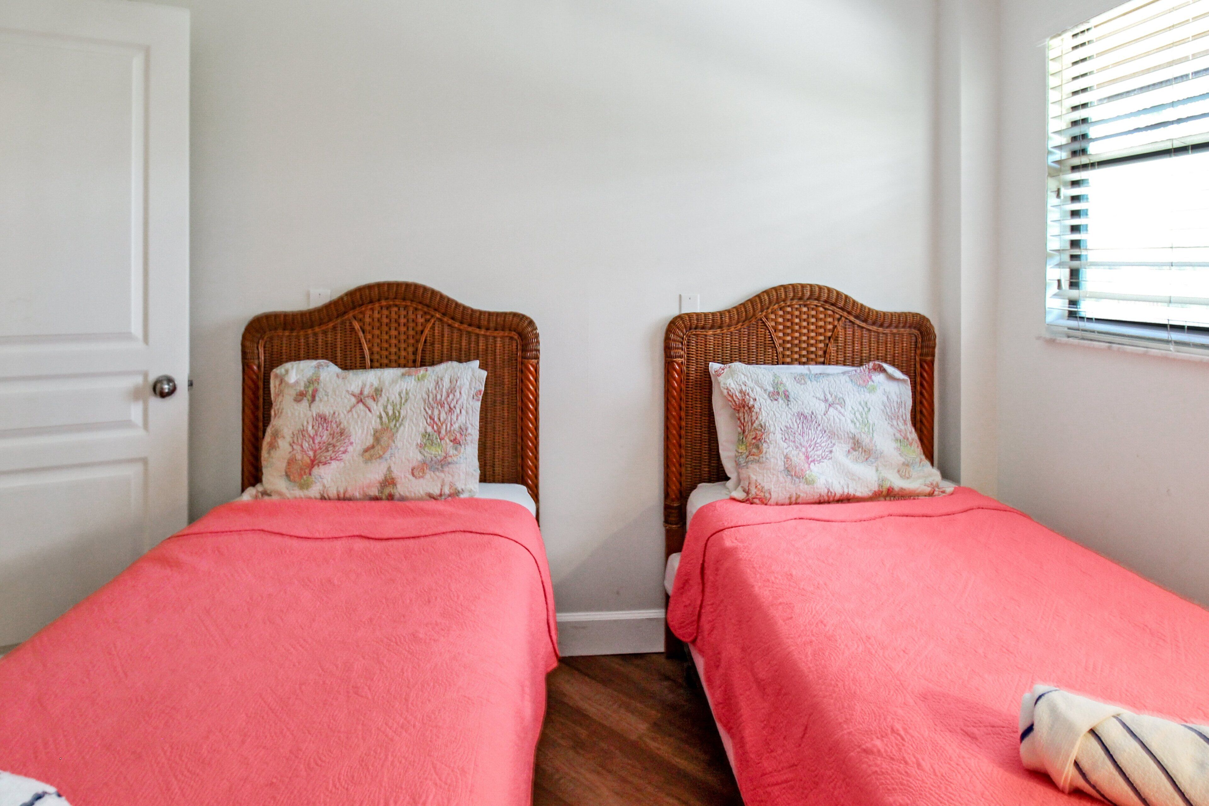 A room with two single beds with matching headboards and footboards, a white door, and a window with blinds.