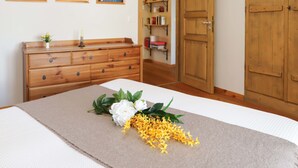 A bedroom with a wooden dresser, a bed with a beige bedspread, and a wooden door.