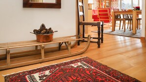 A wooden bench with a copper pot of pinecones, a chair, a patterned rug, and a dining area with a red chair and table.