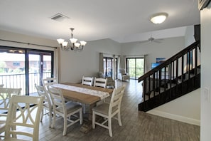 Un comedor con una mesa de madera y sillas blancas, una araña y una escalera que sube a un nivel superior.