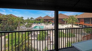 Un área de piscina con sillones de descanso y sombrillas, rodeada de palmeras y edificios con techos marrones.