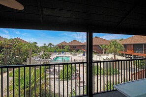 A pool area with lounge chairs and umbrellas, surrounded by palm trees and buildings with brown roofs.