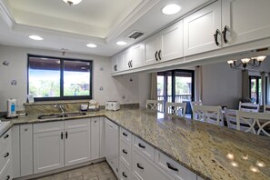 A kitchen with white cabinets, a granite countertop, a window, and a dining area with chairs.
