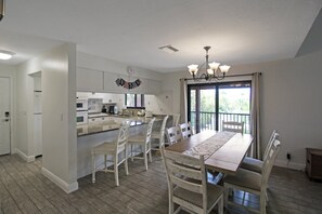 A spacious kitchen with white cabinetry, a dining area with a wooden table and chairs, and a large window with a view of greenery.