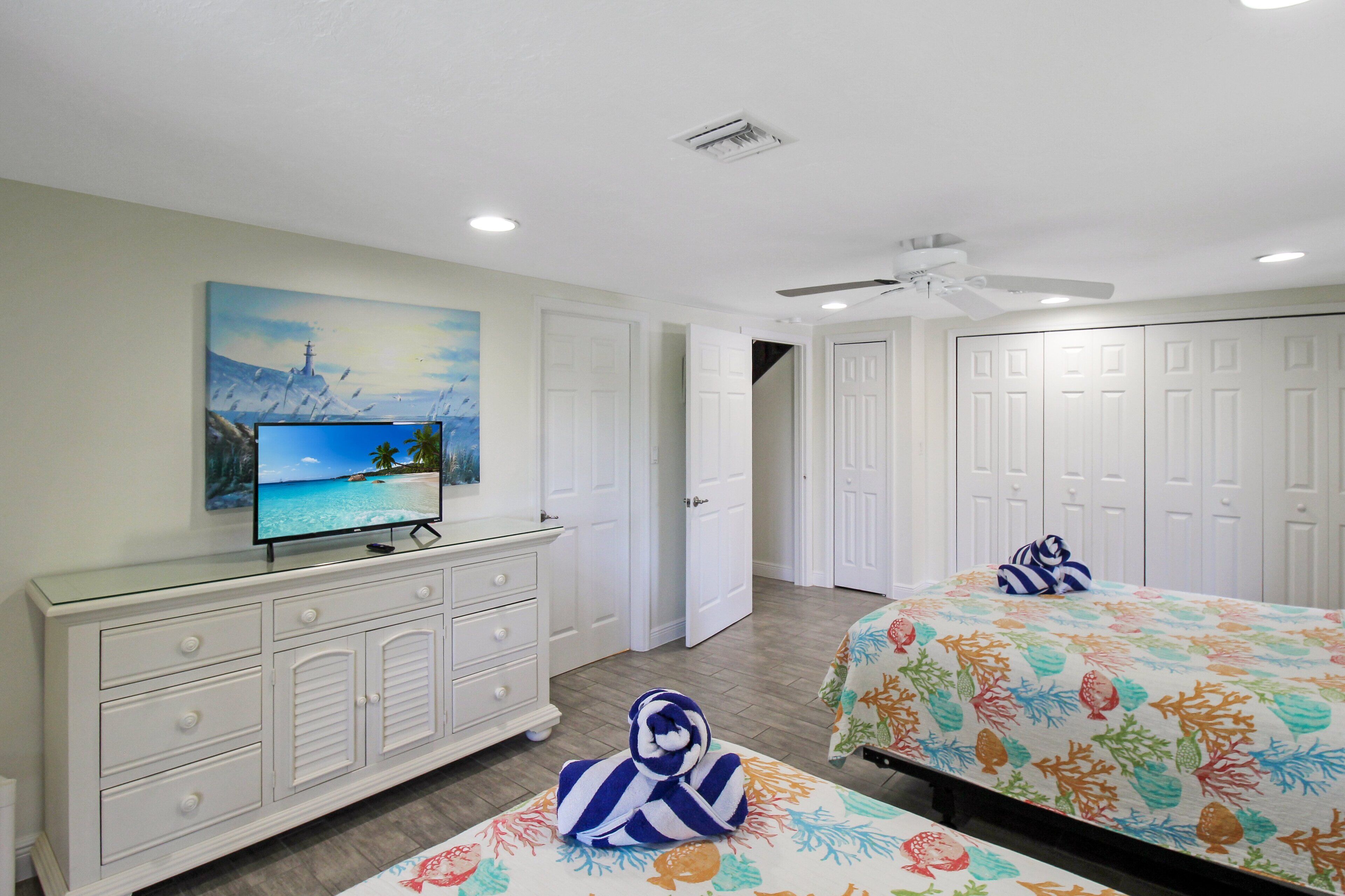 A hotel room with a bed, a TV on a dresser, a painting on the wall, and a ceiling fan.