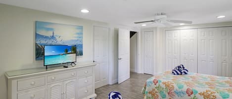A hotel room with a bed, a TV on a dresser, a painting on the wall, and a ceiling fan.
