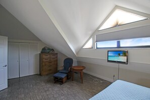 A bedroom with a sloped ceiling, a bed, a chair, a small table, a TV, and a wardrobe.