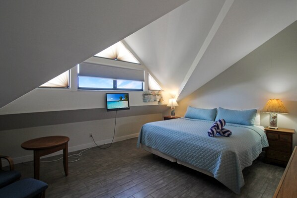 Un dormitorio con una cama, un televisor en la pared, una ventana y una mesita de noche con lámpara.