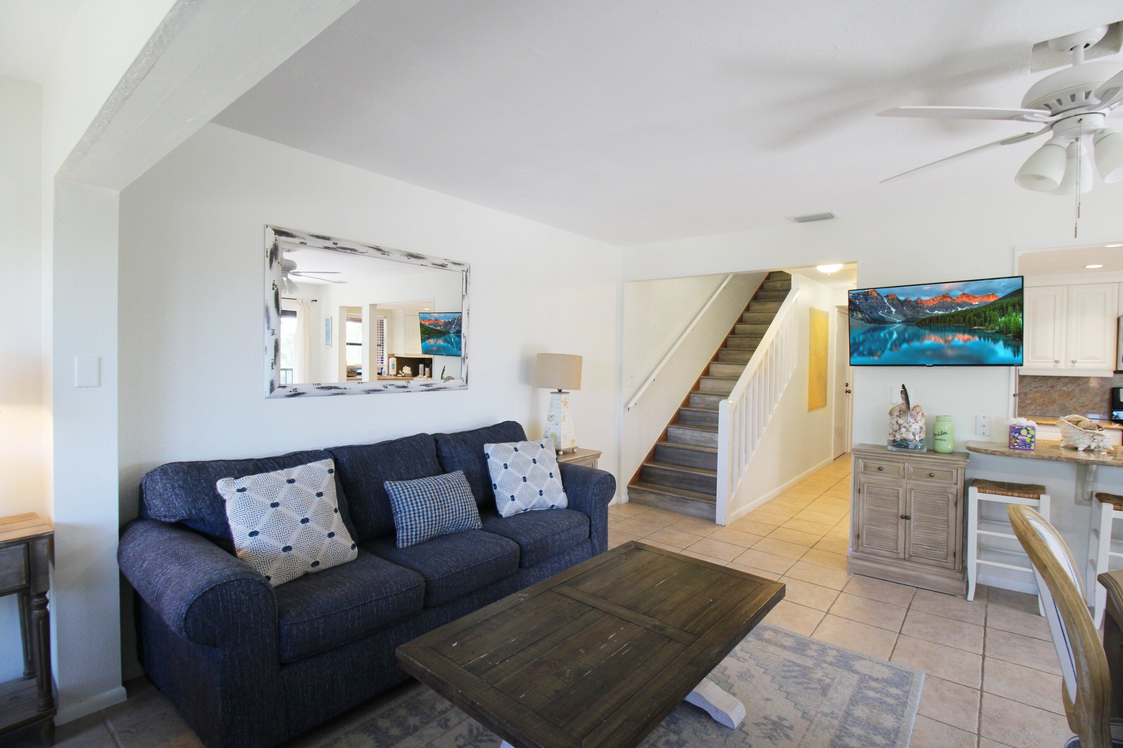 Ein Wohnzimmer mit einer Couch, einem Couchtisch und einem Fernseher. Eine Treppe führt zu einer Küchenzeile.