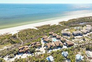 An aerial view of a coastal resort with multiple buildings, a beach, and a clear view of the ocean.