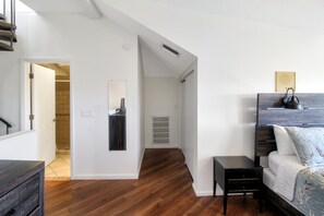 A modern living room with a wooden floor, a white wall, a small black side table, a white sofa with a floral throw, and a large mirror. - Pet friendly 3BR Villa with Gulf Views & Rooftop Sundeck - Private Beach - Signal Inn 17 (Sanibel)