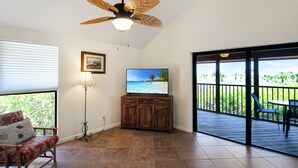 A room with a ceiling fan, a television on a wooden cabinet, a chair, and a view of a balcony with a table and chairs. - Pet friendly 3BR Villa with Gulf Views & Rooftop Sundeck - Private Beach - Signal Inn 17 (Sanibel)